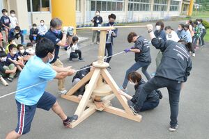 巨大なまいぎり式の火起こしに挑戦する児童と教員、市職員たち